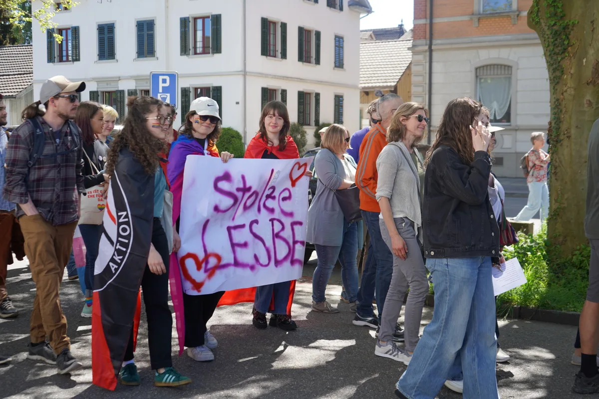 Man sieht Personen an einer Demonstration und ein Transparent. Darauf steht: Stolze Lesbe.